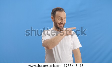 Young man pointing with his finger in the advertising space on the right of the screen. Indoor studio shot isolated on blue background. 