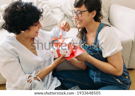 Woman opening the gift given by her girlfriend. Lesbian couple sitting together and opening a gift.