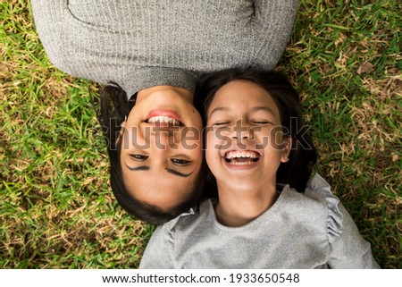 Little girl laughing with her mother lying head to head on the grass. Royalty-Free Stock Photo #1933650548