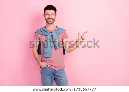 Photo of happy cheerful young guy point finger empty space hold hand pocket isolated on pastel pink color background
