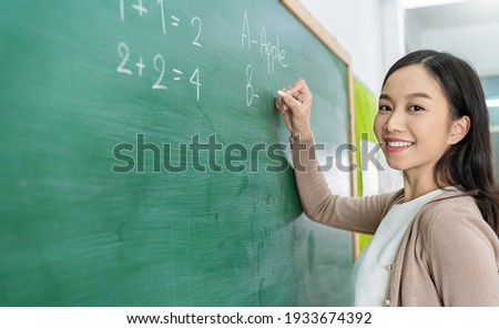 Closeup portrait of young happy asian teacher write on chalk board. Woman writing on blackboard wall. Idea creative education teaching math and spelling letter, knowledge, back to school concept