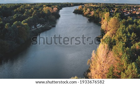 Cityscape at river shore aerial. Autumn nobody nature landscape. Colorful leafy trees forest at sun day. Cottages at city streets. Urban buildings at downtown suburbs. Green grass valley stream shore