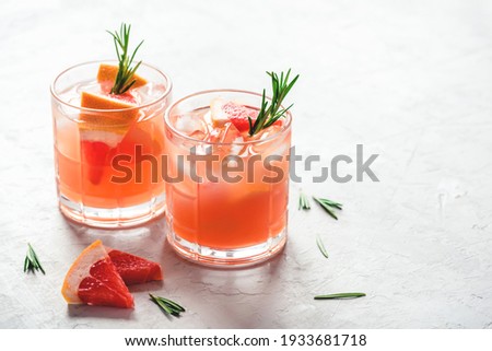 Refreshing grapefruit cocktail with ice and rosemary on a grey background. Royalty-Free Stock Photo #1933681718