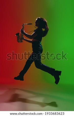 Silhouette of young girl with saxophone posing isolated on green-red background.