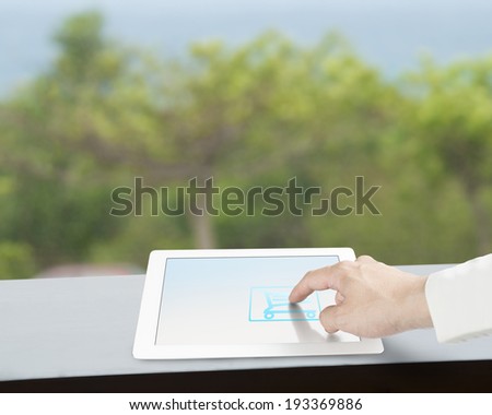 Touching tablet with shopping cart icon on screen nature background