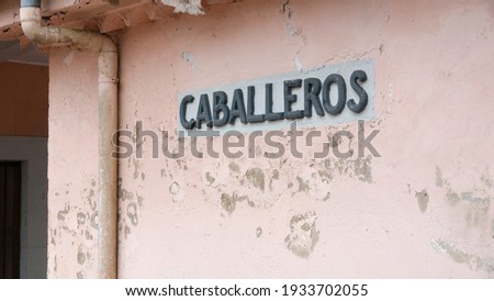 Gentlemen in spanish "caballeros" sign in weathered pink wall