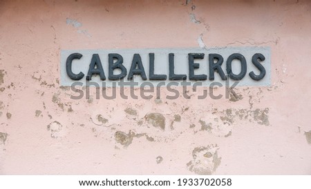 Gentlemen in spanish "caballeros" sign in weathered pink wall