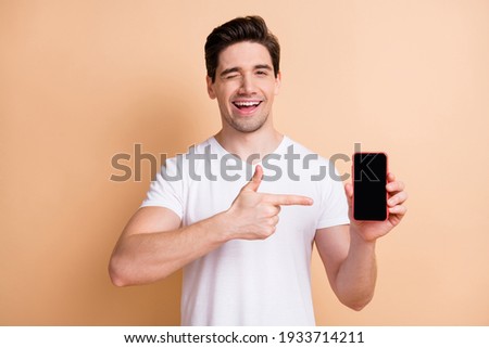 Portrait of positive handsome person eye wink direct finger empty space display isolated on beige color background