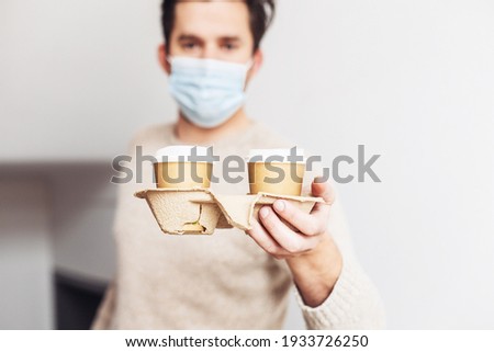 Delivery man in a medical mask giving two take away coffee cups in a cardboard holder 
