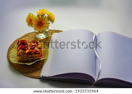 Spring breakfast, lunch - a piece of cake, a cupcake, a cake on a jute stand. A cup of flowers with yellow dandelions. On white background. View from above. And an open notebook
