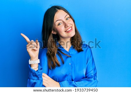Young brunette woman wearing casual blue shirt with a big smile on face, pointing with hand and finger to the side looking at the camera. 