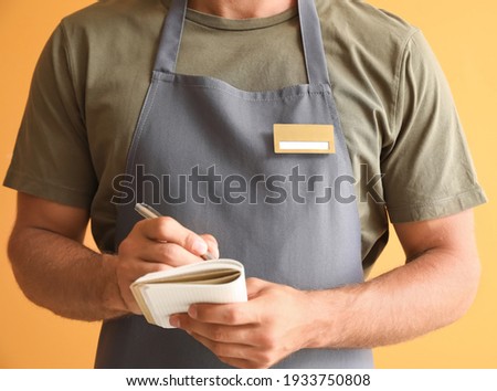 Male waiter with blank badge on color background Royalty-Free Stock Photo #1933750808