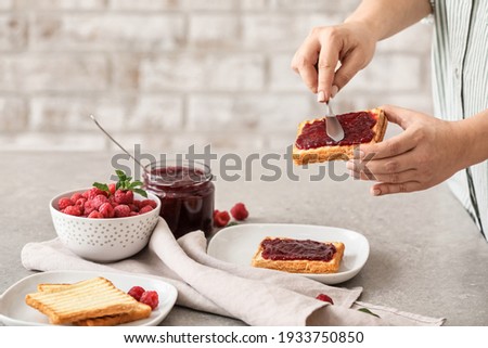 Woman spreading sweet raspberry jam on toast in kitchen Royalty-Free Stock Photo #1933750850