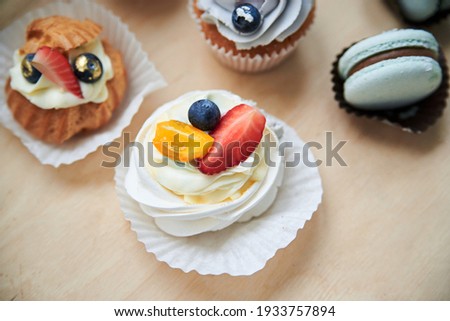 Close-up picture of baked cupcakes with cream cheese icing and fruits on top, mint macarons. Colorful sweet pastries on wooden table buffet. Festive holiday celebration. party. Fancy mini desserts.