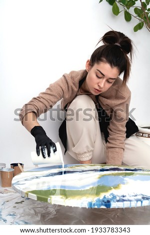 A young woman creates a painting using liquid art technique. Artistic background. Round canvas with dripping acrylic paint.