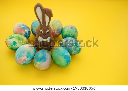 Chocolate Easter bunny lies with colorful eggs on a yellow background, close-up