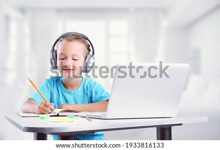 Smiling little child wearing headphones sitting at the table, studying at home,