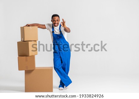 courier, a young African-American in a blue jumpsuit and white T-shirt, tired, standing near the paper boxes folding them, working. Isolated on white background. The concept of delivery, mail, deliver