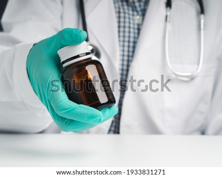 A doctor wearing gloves and holding a brown glass bottle with copy space for text. Close-up photo. Concept of medical and healthcare.