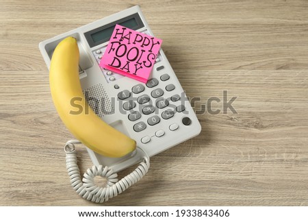 Corded phone with banana as handset and words Happy Fool's Day on wooden table, above view. Space for text