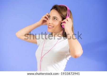 Photo of happy positive optimistic young woman posing isolated over purple background listening music with headphones.