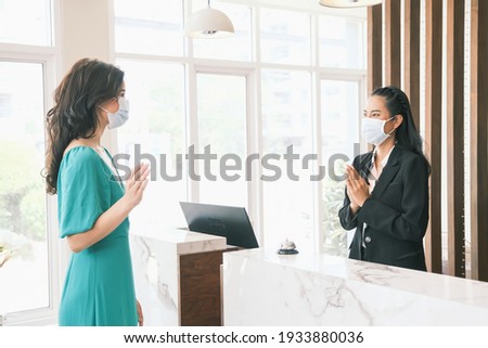 Asian girl receptionist and Caucasian woman traveler wearing medical masks checking or checkout in hotel, New normal tourist concept Royalty-Free Stock Photo #1933880036