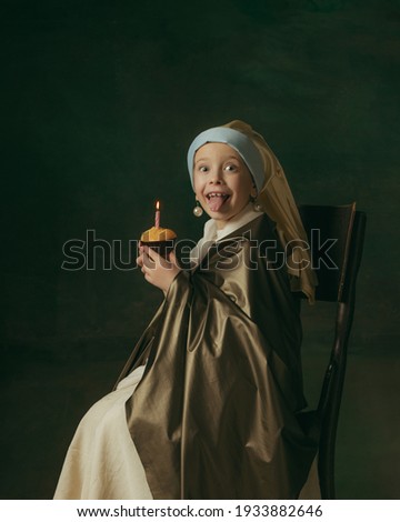 Birthday cake. Medieval little girl as lady with a pearl earring on dark studio background. Concept of comparison of eras, childhood, ancient. Stylish, creative, art vision, new look of artwork.