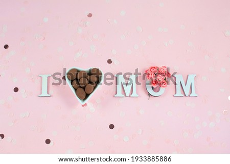 Wooden letters in the phrase I love mom with flowers and chocolate candy on a pink background. Greeting card concept for mother day.