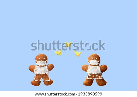 Cute gingerbread couple with protective face masks and butterflies, isolated, blue background. Greeting card, copy space for text. Creative concept in coronavirus (COVID-19) time