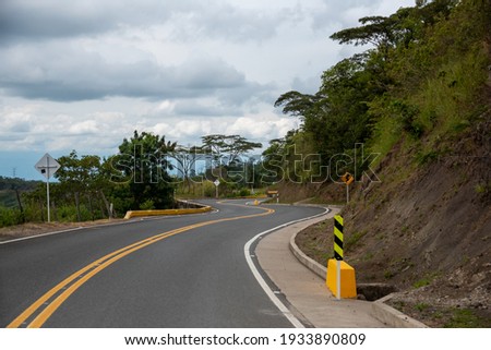 Rural road with curves and signs in a warm climate zone in Colombia. Royalty-Free Stock Photo #1933890809