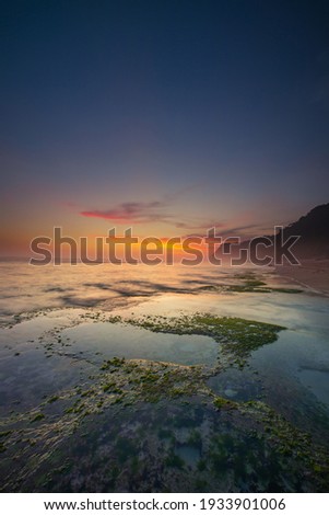Seascape for background. Sunset time. Beach with rocks and stones. Low tide. Stones with green seaweed and moss. Blue sky with motion clouds. Slow shutter speed. Copy space. Melasti beach, Bali