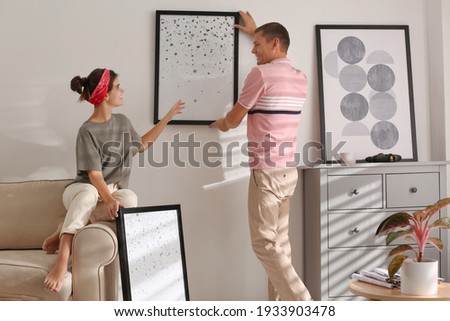 Couple decorating room with pictures together. Interior design Royalty-Free Stock Photo #1933903478