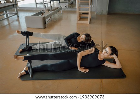 Two sporty women doing toning pilates exercise for legs with Magic circle, Pilates Yoga Ring in a big Fitness studio, center, gymnasium, health club with Reformer equipment. Personal trainer class.
