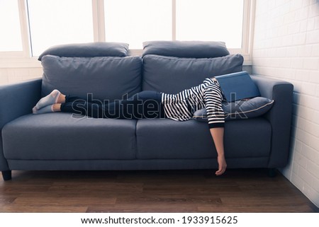 Young millennial Asian woman student at home quarantine bored reading book falling asleep on coach with book covering head, feeling lazy sleepy procrastination on working studying educational learning Royalty-Free Stock Photo #1933915625