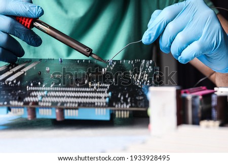 Technician repairing electronic circuit board with soldering iron at table, closeup Royalty-Free Stock Photo #1933928495