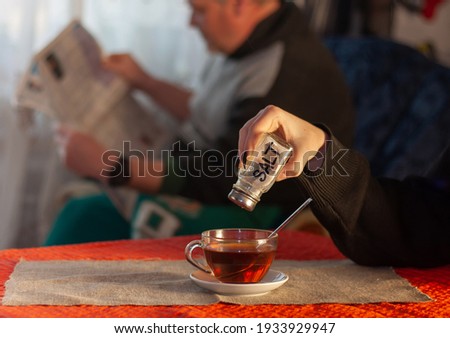 April fools day joke: Girl pours salt into tea while father reads newspaper Royalty-Free Stock Photo #1933929947