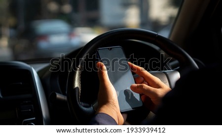Simulated picture of the driver's hand using a smart phone, black screen inside the car, locating through a near-distance GPS navigation application, parked on the side of the road.