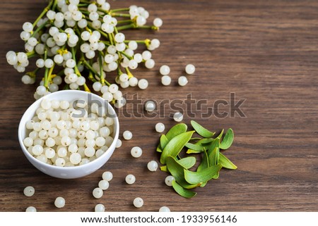 container with mistletoe fruit and branches of evergreen white mistletoe on a wooden surface