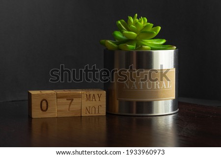 May 07. Image of the May 07 calendar of wooden cubes and an artificial plant on a brown wooden table reflection and black background. with empty space for text
