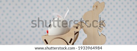 A wooden rabbit carries a cart with an egg with bunny ears. Easter decorations.