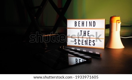 Behind the scenes text on letterboard Lightbox or Cinema Light box. Movie clapperboard or film slate megaphone and director chair beside. Background LED color. shoot in video production studio.