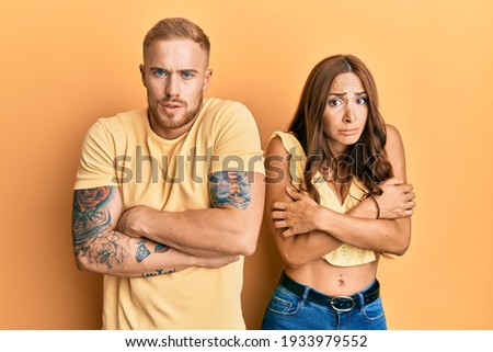 Young couple of girlfriend and boyfriend hugging and standing together shaking and freezing for winter cold with sad and shock expression on face 