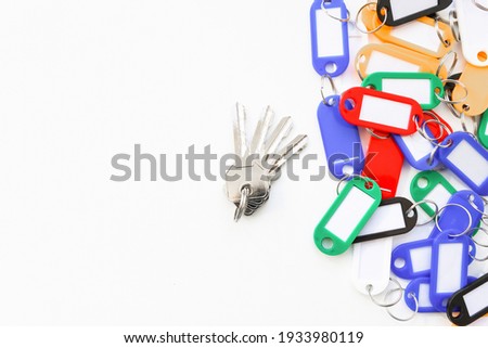 A bunch of keys made of metal on a gray background. A bunch of tags of different colors with a place for the inscription.