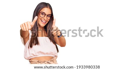 Young hispanic woman wearing casual clothes and glasses approving doing positive gesture with hand, thumbs up smiling and happy for success. winner gesture. 