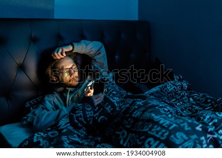 A young man addicted to social media checking his phone before going to bed, Addiction, social media, after dark concept Royalty-Free Stock Photo #1934004908