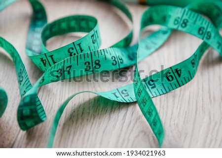 Close up picture of green measure tape on wooden background. Weight loss, diet concept - web banner of a measuring tape, copy space. Health Nutrition and Obesity Concept. Sewing concept.