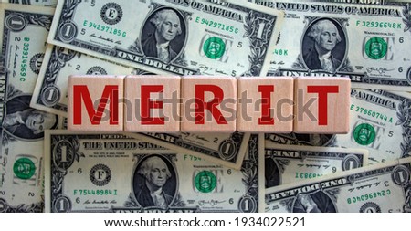 Merit symbol. Wooden cubes with the word 'merit'. Beautiful background from dollar bills, copy space. Business and merit concept.