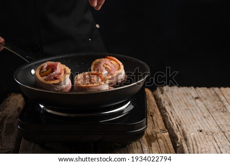 Cooking steak, chops with beef bacon on a grill pan by hands of a chef on a black background for copy space text restaurant menu