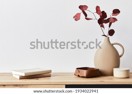 Minimalist concept of living room interior at elegant apartment with wooden commode, leaf in ceramic vase and elegant personal accessories in modern home decor. Copy space. Template. .