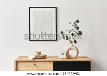 Stylish interior of living room with mock up poster frame, wooden commode, book, leaf in ceramic vase and elegant personal accessories. Minimalist concept of home decor. Template.